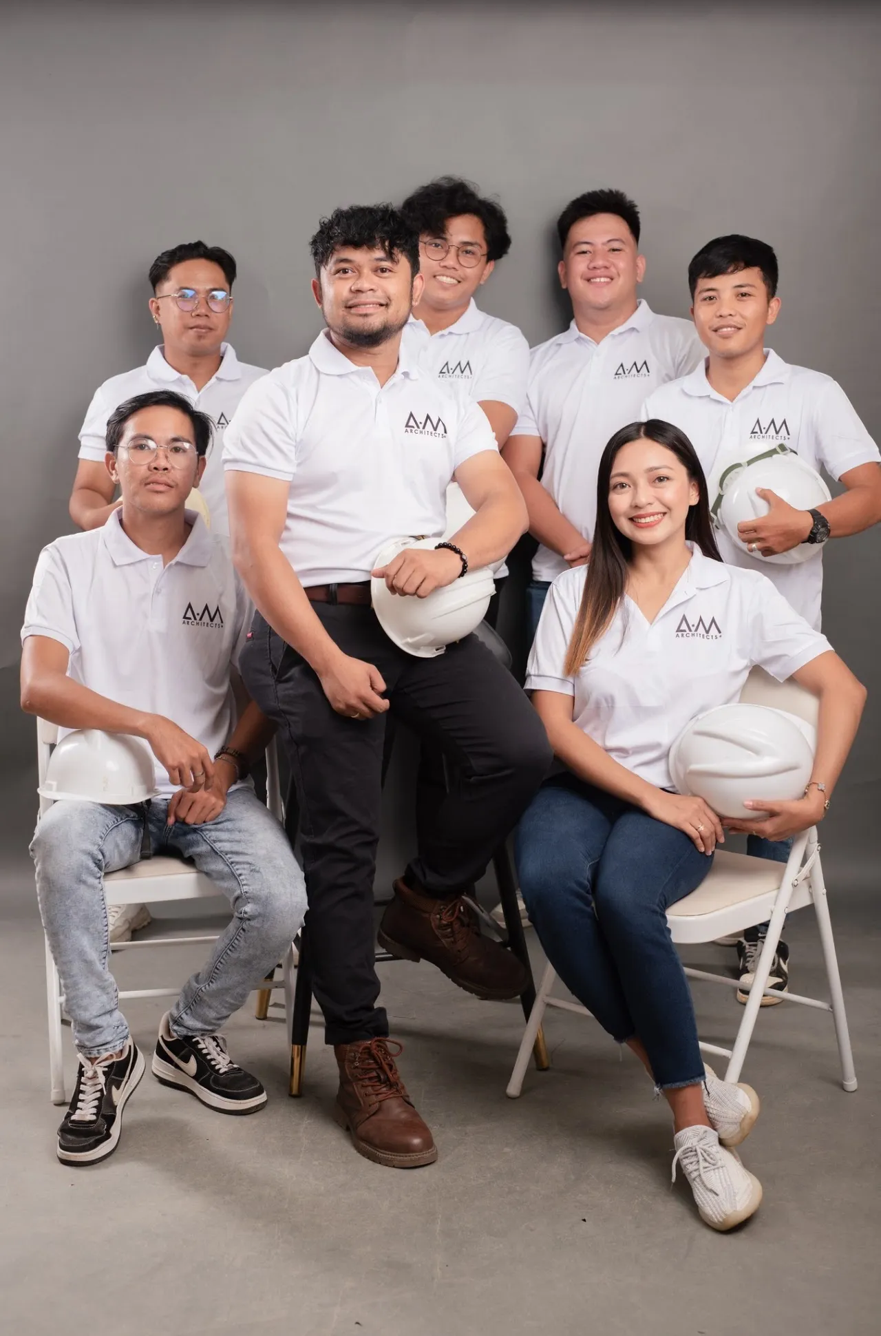 The A.M Architects+ team in white polos holding hard hats, posed together in the studio